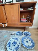 Overview showing four Delft plates on floor and wine glasses, bells on shelf