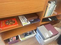 Books on lower shelf including Betty Crocker’s Cookbook and others; boxes of CDs/DVDs below