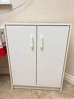Front view of closed white laminate cabinet with two doors and plastic handles