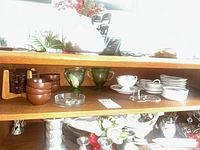 Full shelf showing coasters, bowls, green glass pieces, teacups and saucers