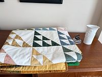 Folded quilt, vase, inkwell on wood surface