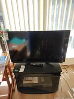 Sharp TV front view on stand with remotes visible