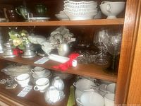 Shelf with pewter candle holders, jigger, wine glasses, pressed glass dishes, candles, tray and linens