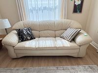 Front view of cream leatherette 3 seat sofa with two accent pillows