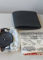 Foam sleeve filter, plastic retainer disc in packaging, folded paper packaging visible