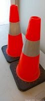 Two orange traffic cones standing upright on table, showing color, reflective bands and bases