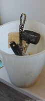 Bucket containing rubber mallet, perforated strap and miscellaneous hardware