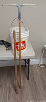 Overall lot: pail, long-handled tools leaning, paintbrush, grey brackets