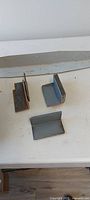 Three individual steel L-brackets displayed on table