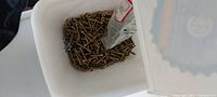 Top view of bin filled with yellow passivated screws and small bag of additional hardware