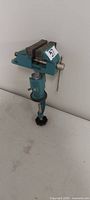 Front view of teal clamp-on bench vise showing jaws, swivel head and clamp base