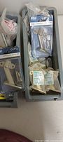 Two grey trays with carded stainless hardware pieces, screws, plugs