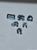 six faceted aquamarines arranged on surface
