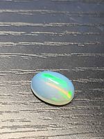 Oval translucent opal on dark background, showing green play-of-color