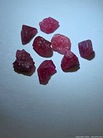 Eight rough deep pink-red spinel crystals on light background