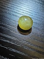 Oval cabochon apatite on tabletop showing color and chatoyancy