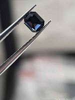 Close-up of faceted spinel held in tweezers, showing deep blue color and cut
