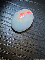 Oval cabochon opal on dark wood showing color play
