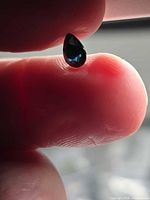 Pear-cut deep blue spinel held between fingers showing color and cut