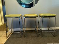 Front view of three green upholstered metal stools