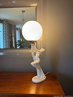 Full view of ceramic figural lamp with globe shade on wood surface