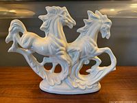 Front view of glossy white ceramic figurine showing two rearing horses and integrated base
