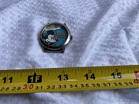 Front view of watch case next to tape for scale