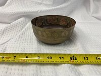 Side view of brass bowl showing engraved exterior and tape for scale