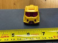 Front view of yellow Hot Wheels Rennes Rig toy car with ruler for scale