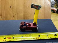 Side view of red Hot Wheels fire truck with yellow boom extended and tape measure for scale