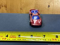 Top/front view showing red body, blue engine, overall size against ruler