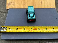 Top view of teal Hot Wheels truck on scale surface with tape measure showing size