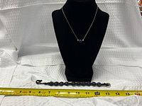 Full view of necklace on bust and bracelet below with tape measure