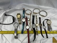 Entire group of 14 watches laid out on fabric with tape for scale