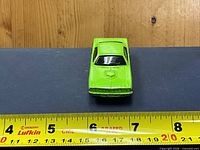 Front view of green die-cast car against ruler showing length
