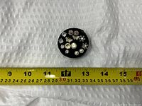 All earrings grouped on round black pad with measuring tape for scale