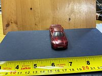 Front view of red die-cast toy car on ruler