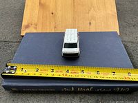 Front view of white die-cast van on book with tape for scale