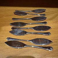 All eight Godinger spreader knives laid out on wooden surface