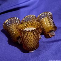 Four amber diamond point peg votive holders on purple fabric