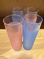Four tall frosted glasses, two blue, two pink, grouped on wooden surface