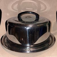 Side view of chrome cake carrier showing lid and base