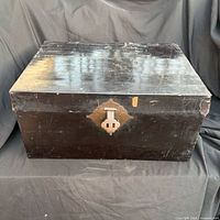 Closed trunk showing black lacquer finish, brass hasp, surface scratches and chips