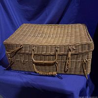Closed wicker suitcase basket front view showing handle and toggles