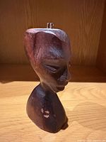 Front left profile of wooden female bust showing facial features and peg on top