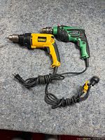 DeWalt and Hitachi corded drills coiled on surface
