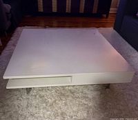 Overall view of white square IKEA coffee table on rug showing shelf opening and legs