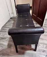 Full view of bench showing dark brown faux leather, tufted seat, flared armrests, wooden legs