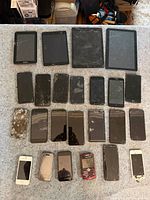 Front view showing cracked screens on four tablets and twenty smartphones