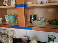 Cabinet shelf showing pitcher, mug, bud vase, small jar, tumbler, tea bag caddy, tray, juicer